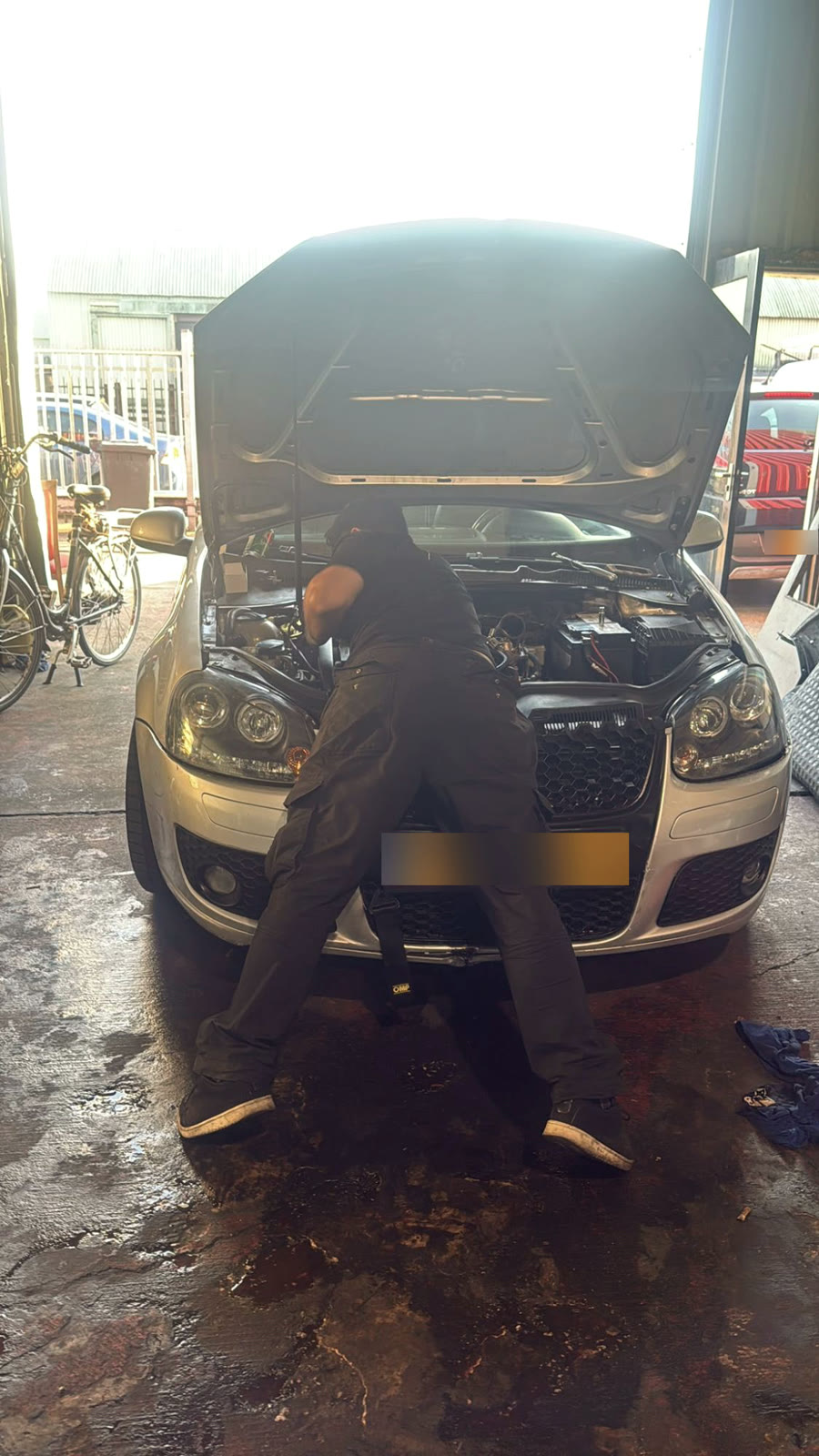 A mechanic working in the engine bay of a Volkswagen Golf
