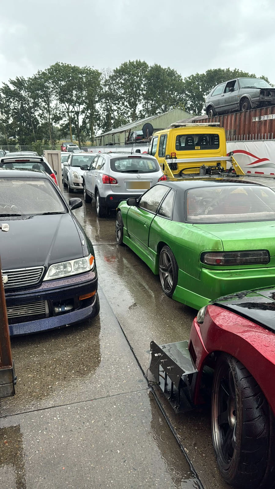 The workshop yard with a green Nissan S13 and everyday cars in the rain